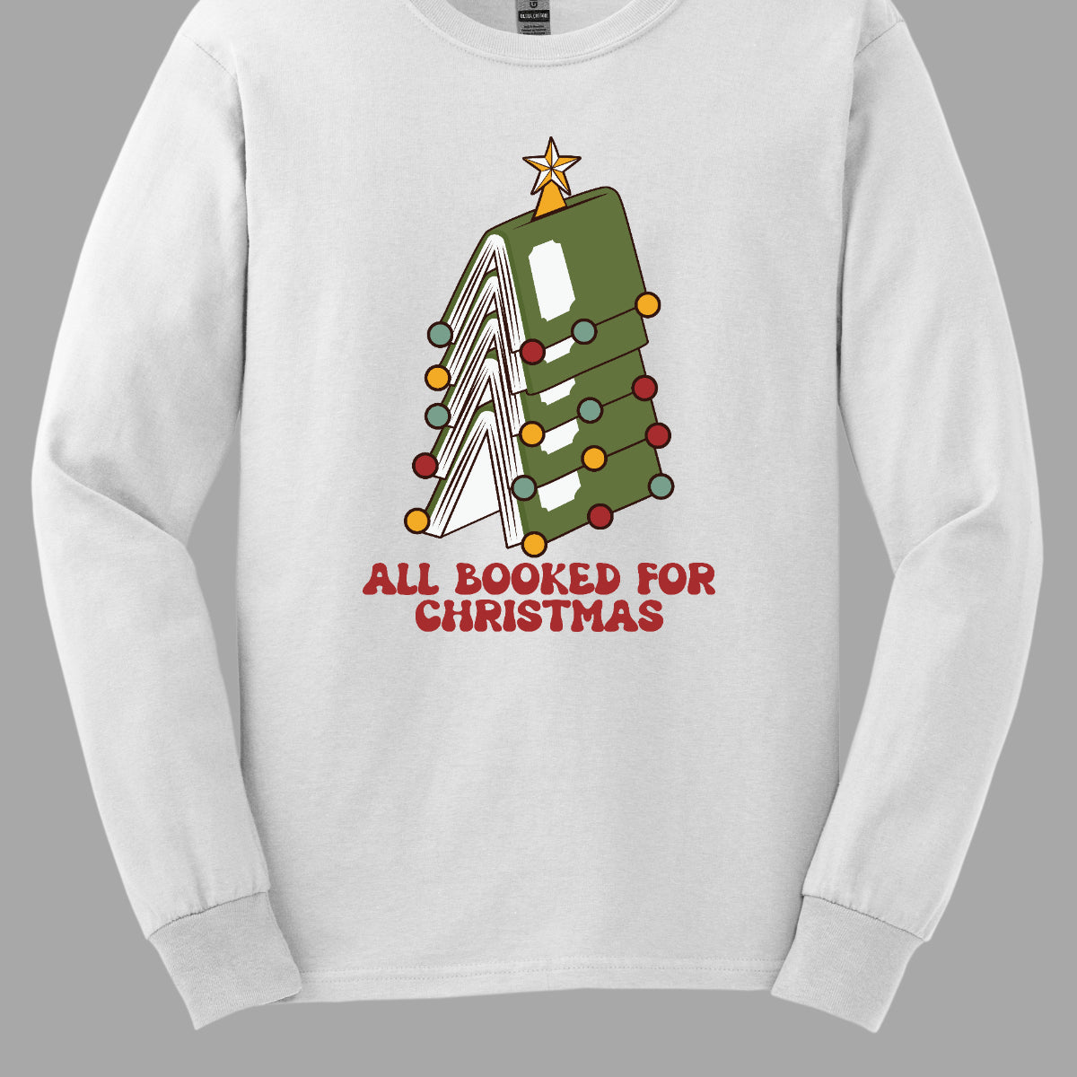 This whimsical t-shirt features the playful phrase "All Booked for Christmas" in a bold, red bubbly font that captures the festive spirit. Above the text, a delightful image showcases a stack of green books, artfully arranged to resemble a decorated Christmas tree. Shop Gorgeousware.com