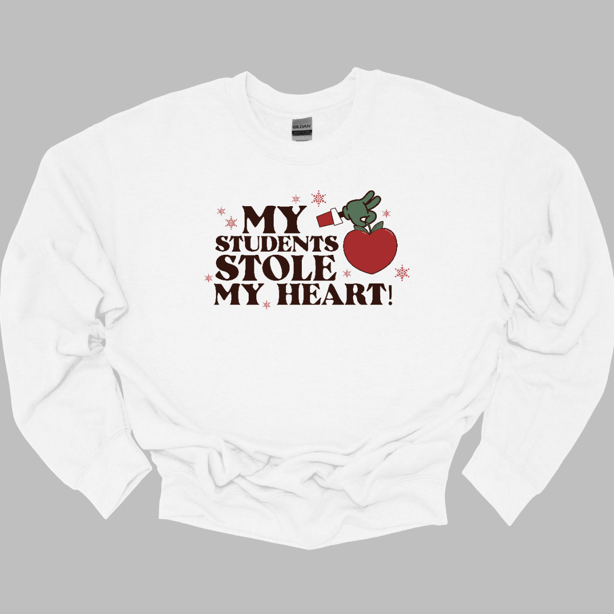 This playful t-shirt features the phrase "My students stole my heart" in fun, whimsical lettering that captures the spirit of teaching. Below the text, a cheeky illustration of the Grinch's green arm emerges, playfully grasping a shiny red apple, symbolizing knowledge and education. Shop at Gorgeousware.com