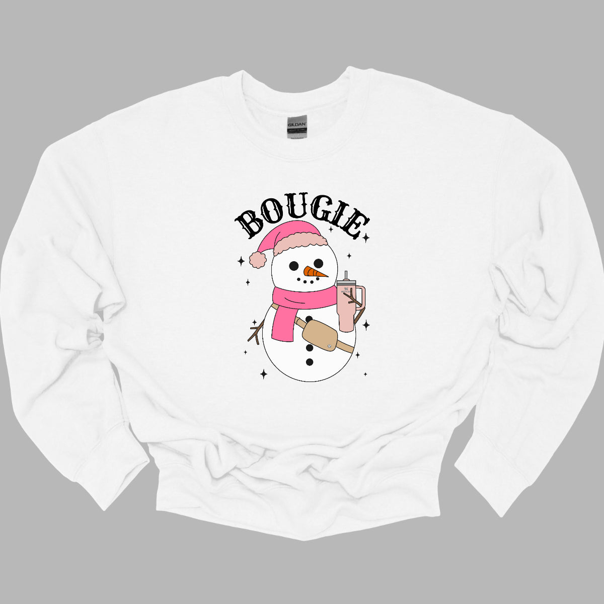 This chic t-shirt features the word "BOUGIE" in elegant, fancy lettering, capturing a stylish vibe. Beneath the text is a charming illustration of a snowman, decked out in a cute pink hat and scarf, exuding festive flair. The snowman is holding a pale pink Stanley cup, adding a trendy touch, while a beige Lululemon belt bag rests around its waist, complete with sparkles that catch the eye and enhance the glamorous theme. Shop Gorgeousware.com