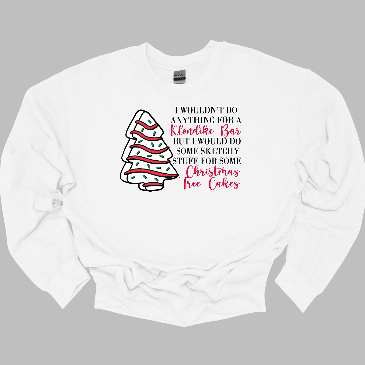 This fun t-shirt features a playful phrase: "I wouldn't do anything for a Klondike Bar but I would do some sketchy stuff for some Christmas Tree Cakes." The main text is presented in a sleek, professional black font, offering a clean contrast to the whimsical red cursive font used for "Klondike Bar" and "Christmas Tree Cakes," drawing attention to those key phrases. Shop Gorgeousware.com