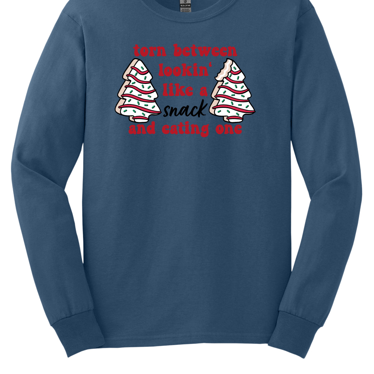 This fun t-shirt features the playful phrase "Torn between lookin' like a snack and eating one" in a vibrant red bubbly font, adding a lively and festive touch. The word "snack" stands out in an elegant black cursive font, creating a nice contrast. Flanking the text are adorable illustrations of Christmas tree cakes on each side, enhancing the holiday spirit and adding a whimsical flair. This shirt is perfect for anyone who loves to celebrate the season with humor and style! Shop Gorgeousware.com