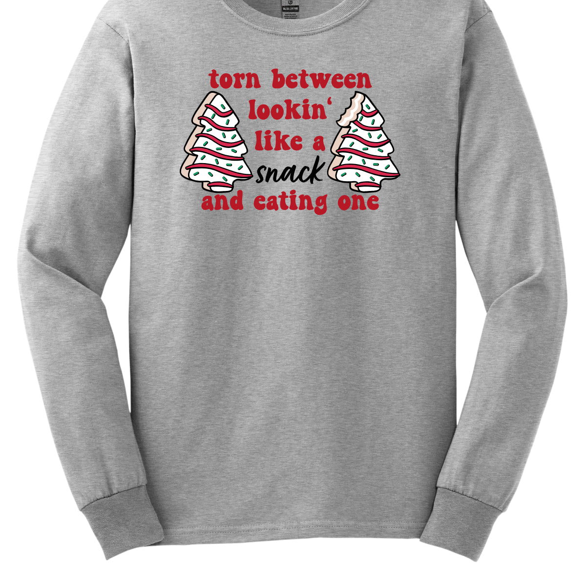 This fun t-shirt features the playful phrase "Torn between lookin' like a snack and eating one" in a vibrant red bubbly font, adding a lively and festive touch. The word "snack" stands out in an elegant black cursive font, creating a nice contrast. Flanking the text are adorable illustrations of Christmas tree cakes on each side, enhancing the holiday spirit and adding a whimsical flair. This shirt is perfect for anyone who loves to celebrate the season with humor and style! Shop Gorgeousware.com