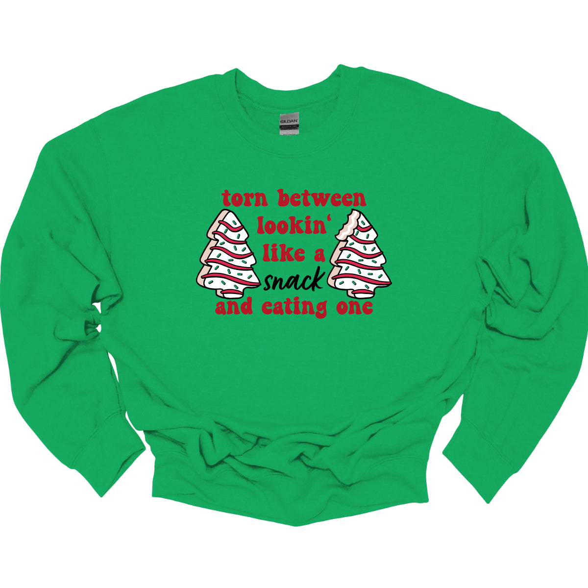 This fun t-shirt features the playful phrase "Torn between lookin' like a snack and eating one" in a vibrant red bubbly font, adding a lively and festive touch. The word "snack" stands out in an elegant black cursive font, creating a nice contrast. Flanking the text are adorable illustrations of Christmas tree cakes on each side, enhancing the holiday spirit and adding a whimsical flair. This shirt is perfect for anyone who loves to celebrate the season with humor and style! Shop Gorgeousware.com