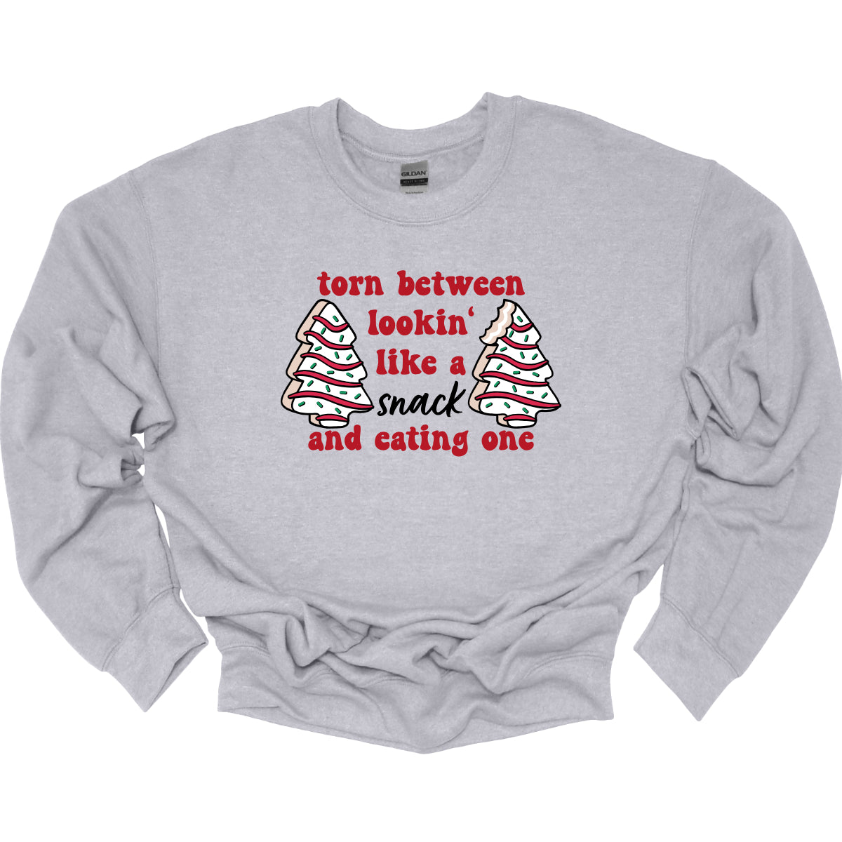 This fun t-shirt features the playful phrase "Torn between lookin' like a snack and eating one" in a vibrant red bubbly font, adding a lively and festive touch. The word "snack" stands out in an elegant black cursive font, creating a nice contrast. Flanking the text are adorable illustrations of Christmas tree cakes on each side, enhancing the holiday spirit and adding a whimsical flair. This shirt is perfect for anyone who loves to celebrate the season with humor and style! Shop Gorgeousware.com