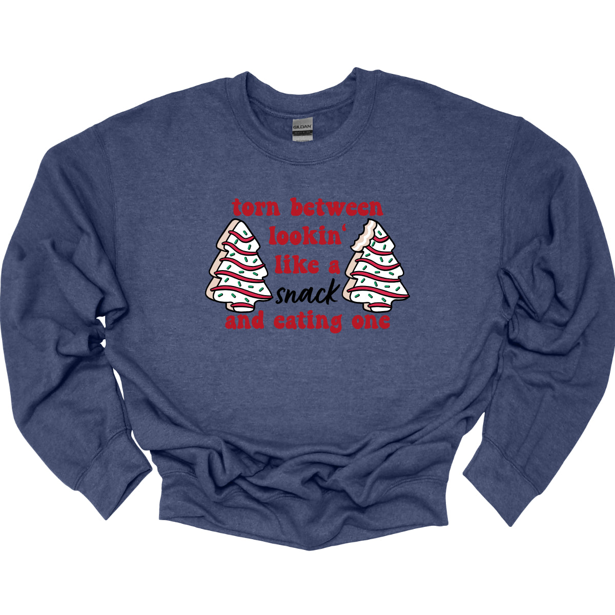 This fun t-shirt features the playful phrase "Torn between lookin' like a snack and eating one" in a vibrant red bubbly font, adding a lively and festive touch. The word "snack" stands out in an elegant black cursive font, creating a nice contrast. Flanking the text are adorable illustrations of Christmas tree cakes on each side, enhancing the holiday spirit and adding a whimsical flair. This shirt is perfect for anyone who loves to celebrate the season with humor and style! Shop Gorgeousware.com