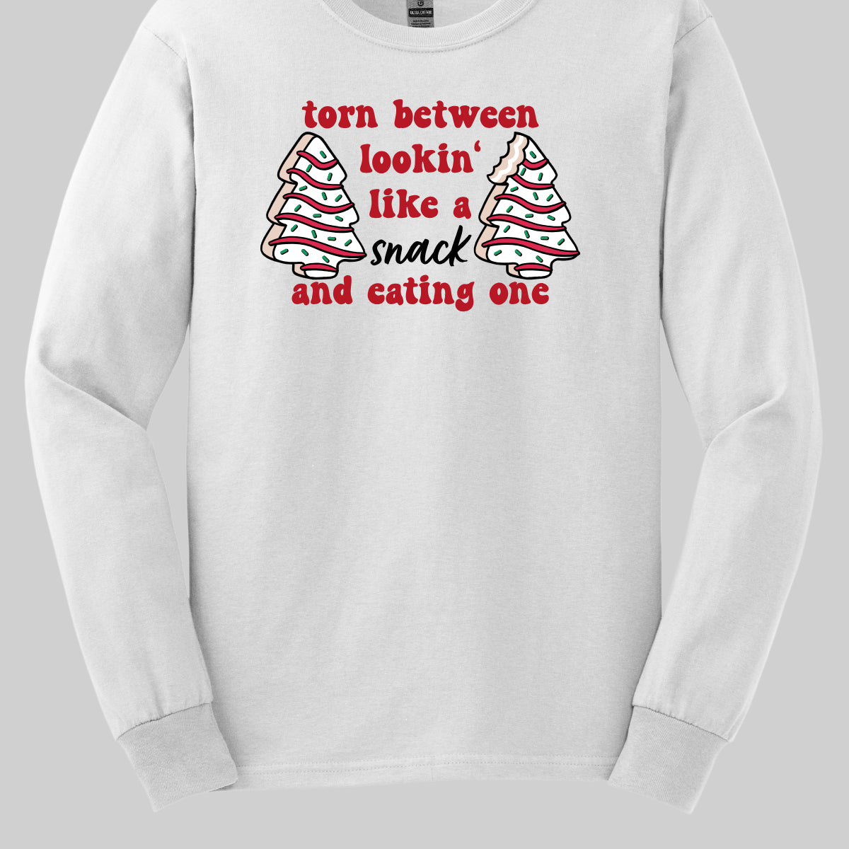 This fun t-shirt features the playful phrase "Torn between lookin' like a snack and eating one" in a vibrant red bubbly font, adding a lively and festive touch. The word "snack" stands out in an elegant black cursive font, creating a nice contrast. Flanking the text are adorable illustrations of Christmas tree cakes on each side, enhancing the holiday spirit and adding a whimsical flair. This shirt is perfect for anyone who loves to celebrate the season with humor and style! Shop Gorgeousware.com