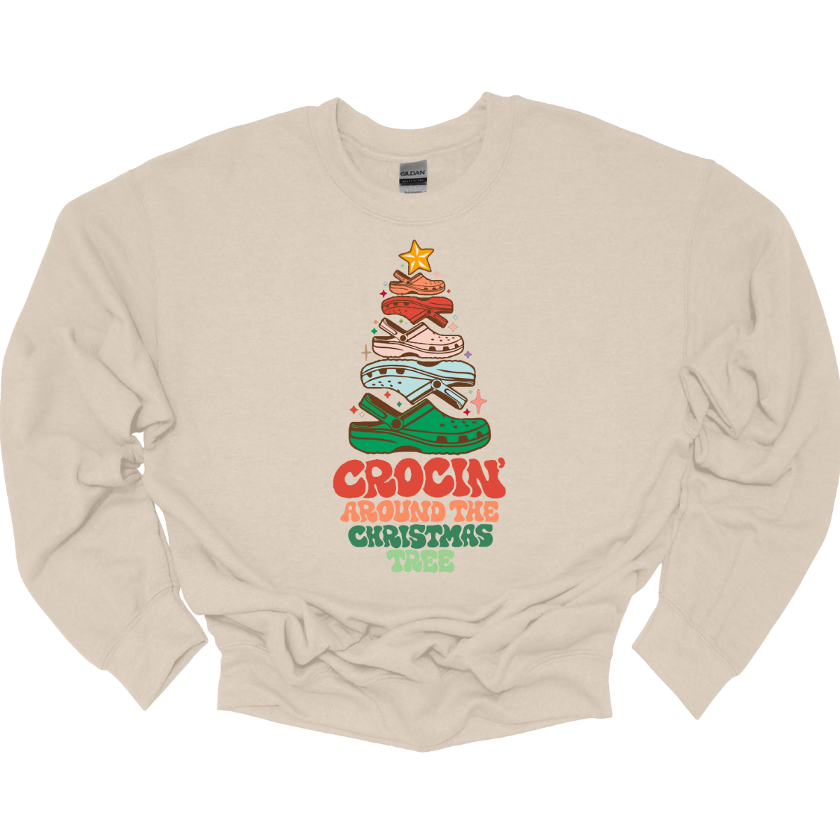 This fun t-shirt features the playful phrase "Crockin' Around the Christmas Tree" in a retro-inspired font that combines vibrant reds and greens for a festive touch. The centerpiece of the design is a whimsical Christmas tree crafted entirely from colorful croc shoes, stacked creatively to form the classic shape. Topping off the tree is a shiny star, adding a delightful finishing touch. Shop at Gorgeousware.com
