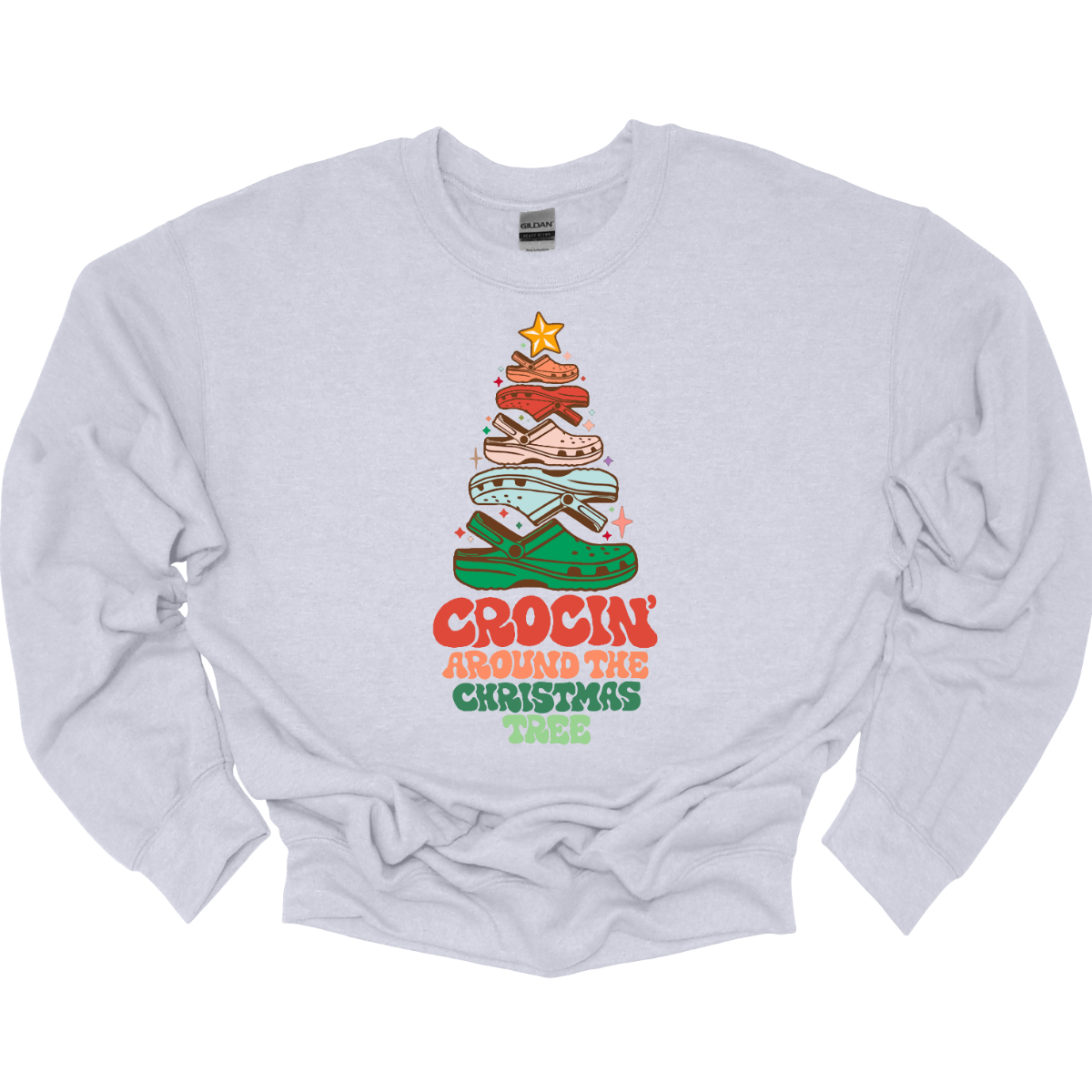 This fun t-shirt features the playful phrase "Crockin' Around the Christmas Tree" in a retro-inspired font that combines vibrant reds and greens for a festive touch. The centerpiece of the design is a whimsical Christmas tree crafted entirely from colorful croc shoes, stacked creatively to form the classic shape. Topping off the tree is a shiny star, adding a delightful finishing touch. Shop at Gorgeousware.com