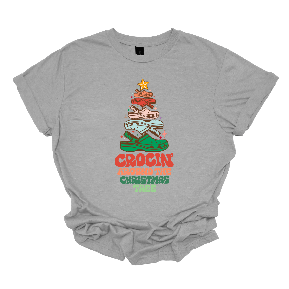 This fun t-shirt features the playful phrase "Crockin' Around the Christmas Tree" in a retro-inspired font that combines vibrant reds and greens for a festive touch. The centerpiece of the design is a whimsical Christmas tree crafted entirely from colorful croc shoes, stacked creatively to form the classic shape. Topping off the tree is a shiny star, adding a delightful finishing touch. Shop at Gorgeousware.com