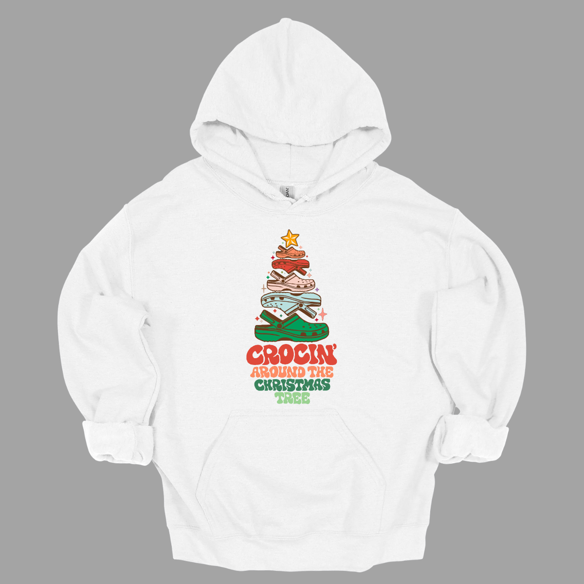 This fun t-shirt features the playful phrase "Crockin' Around the Christmas Tree" in a retro-inspired font that combines vibrant reds and greens for a festive touch. The centerpiece of the design is a whimsical Christmas tree crafted entirely from colorful croc shoes, stacked creatively to form the classic shape. Topping off the tree is a shiny star, adding a delightful finishing touch. Shop at Gorgeousware.com
