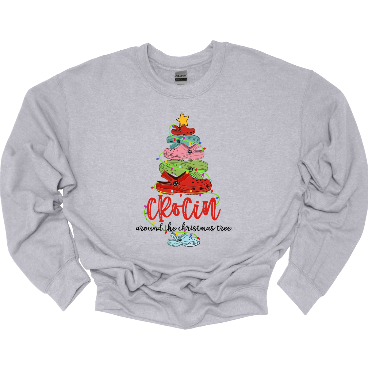 This playful t-shirt features the fun phrase "Crockin' Around the Christmas Tree" with a unique twist. The word "Crockin'" is showcased in a vibrant red cursive font, with playful spaces between the letters, adding a whimsical flair. Below that, the rest of the phrase is written in a smaller, elegant black cursive font, providing a charming contrast. Shop Gorgeousware.com