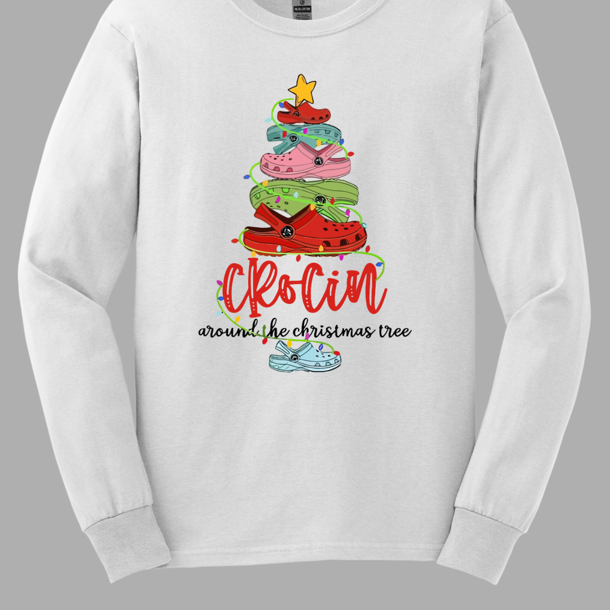 This playful t-shirt features the fun phrase "Crockin' Around the Christmas Tree" with a unique twist. The word "Crockin'" is showcased in a vibrant red cursive font, with playful spaces between the letters, adding a whimsical flair. Below that, the rest of the phrase is written in a smaller, elegant black cursive font, providing a charming contrast. Shop Gorgeousware.com