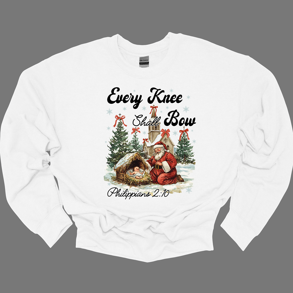 This festive and powerful apparel design features the phrase "Every Knee Shall Bow" in bold, elegant lettering, symbolizing the reverence and humility of the Christmas story. The artwork showcases Santa Claus, traditionally known for his joyful spirit, bowing down in awe before a humble manger that cradles baby Jesus. In the background, an old chapel stands as a symbol of faith, with evergreen trees adorned with festive bows, adding a touch of seasonal beauty and serenity. Shop at Gorgeousware.com
