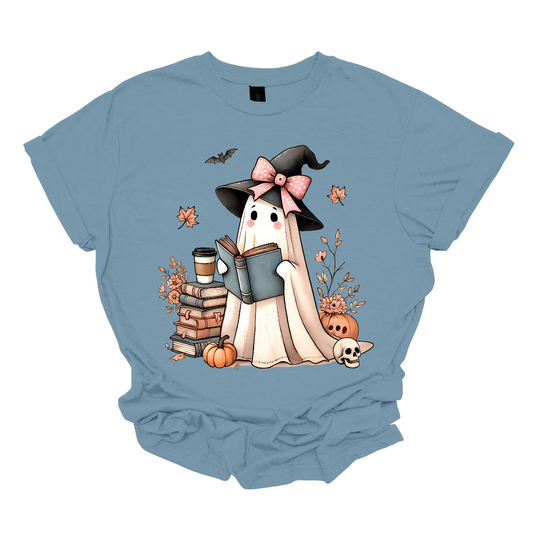This T-shirt features an adorable ghost wearing a witch's hat adorned with a pink bow. The ghost has a warm, friendly expression as she enjoys her coffee, with a stack of books by her side.  Around her, small pumpkins are scattered on the ground, adding a cozy, autumnal vibe. The design perfectly captures the charm of the Halloween season with a cute and whimsical twist. Shop at Gorgeousware.com