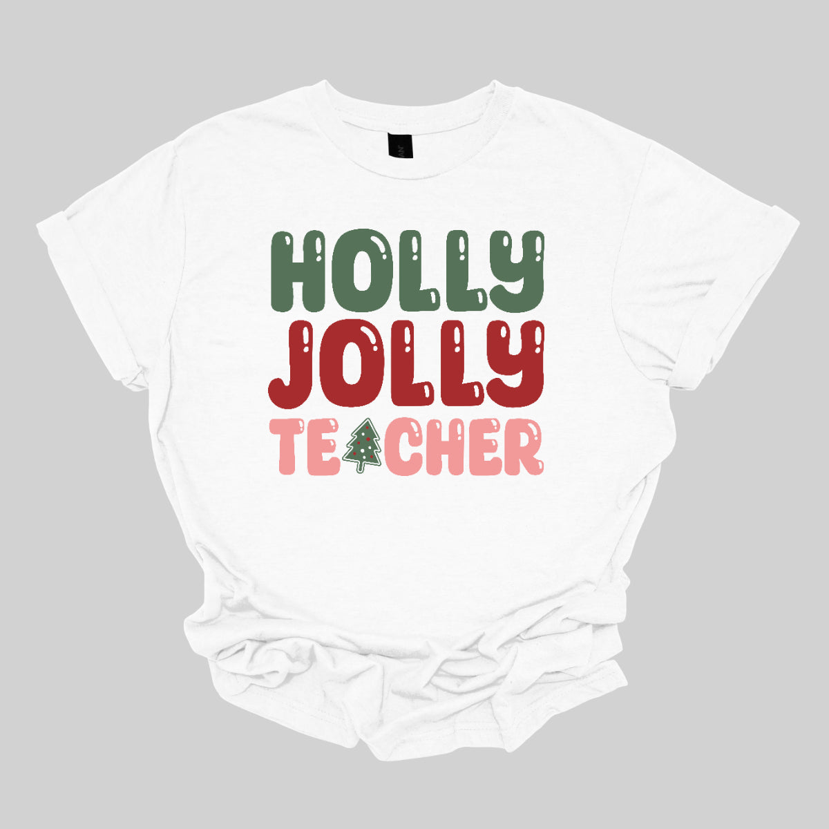 This festive t-shirt features the cheerful phrase "Holly Jolly Teacher" in a delightful bubbly font with fun cut-outs that add a playful touch. The word "Holly" is presented in a vibrant green, evoking the essence of holiday greenery, while "Jolly" pops in a bright red, radiating festive cheer. The word "Teacher" is in a cheerful pink, providing a lovely contrast. A whimsical twist comes with the letter "A" in "Teacher," which is creatively transformed into a charming Christmas tree. Shop Gorgeousware.com