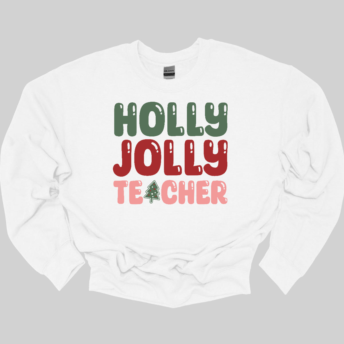 This festive t-shirt features the cheerful phrase "Holly Jolly Teacher" in a delightful bubbly font with fun cut-outs that add a playful touch. The word "Holly" is presented in a vibrant green, evoking the essence of holiday greenery, while "Jolly" pops in a bright red, radiating festive cheer. The word "Teacher" is in a cheerful pink, providing a lovely contrast. A whimsical twist comes with the letter "A" in "Teacher," which is creatively transformed into a charming Christmas tree. Shop Gorgeousware.com