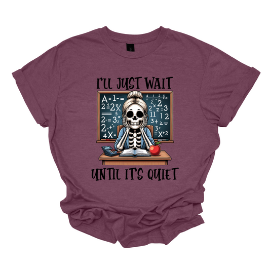 This T-shirt features a skeleton sitting at a cluttered desk, dressed in a cozy cardigan with a messy bun on top of its skull. The skeleton is leaning forward, resting its head on its bony hands as if exhausted or overwhelmed.  The shirt says, "I'll just wait until its quiet".  Shop at Gorgeousware.com