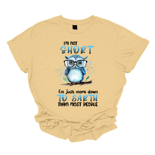 This fun and quirky shirt features the playful message, "I'm not short" at the top and "I'm just more down to earth than most people" at the bottom. The bold print font highlights the words "short" and "to earth" in vibrant blue lettering. The text is divided into two sections, with an adorable blue owl wearing oversized glasses perched on a branch in the center. It's the perfect shirt for those with a great sense of humor and a down-to-earth attitude. Shop now at Gorgeousware.com