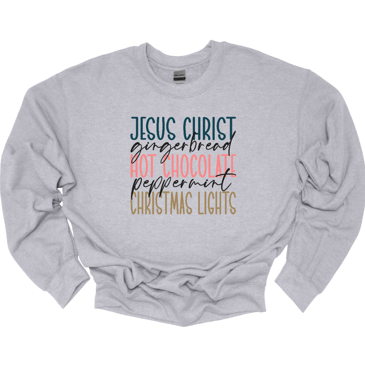 This festive t-shirt showcases a vibrant design with the phrase "JESUS CHRIST," "gingerbread," "HOT CHOCOLATE," "peppermint," and "CHRISTMAS LIGHTS" arranged vertically down the shirt. The words "JESUS CHRIST," "HOT CHOCOLATE," and "CHRISTMAS LIGHTS" are all in bold capital letters, each presented in a different bright color, creating a cheerful and eye-catching effect. Shop Gorgeousware.com