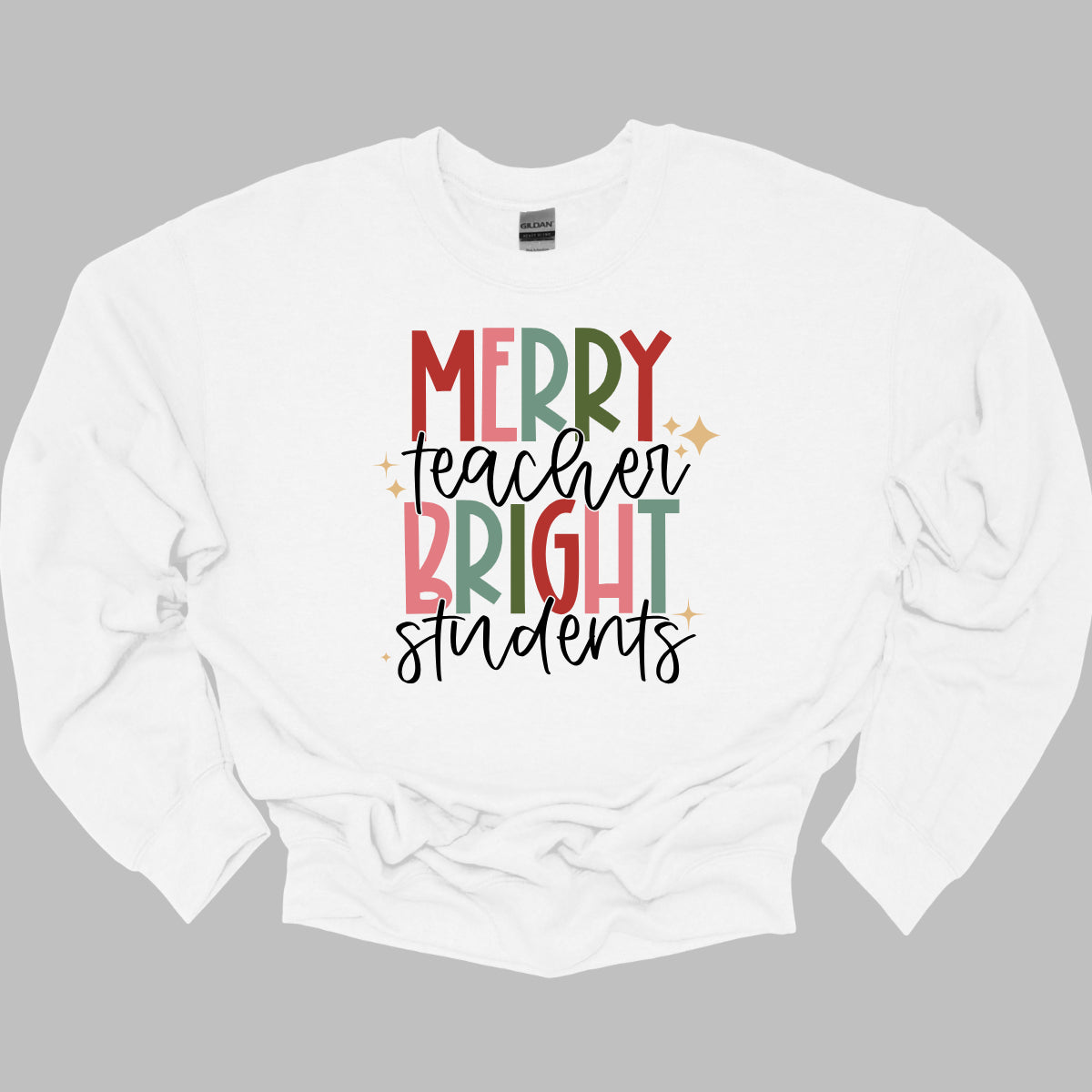 This festive t-shirt showcases the cheerful phrase "Merry Teacher Bright Students" in a delightful design. The words "MERRY" and "BRIGHT" are prominently featured in a blocky yet playful font, with each letter bursting in a vibrant mix of shades of green and red, evoking the spirit of the holiday season. Shop Gorgeousware.com
