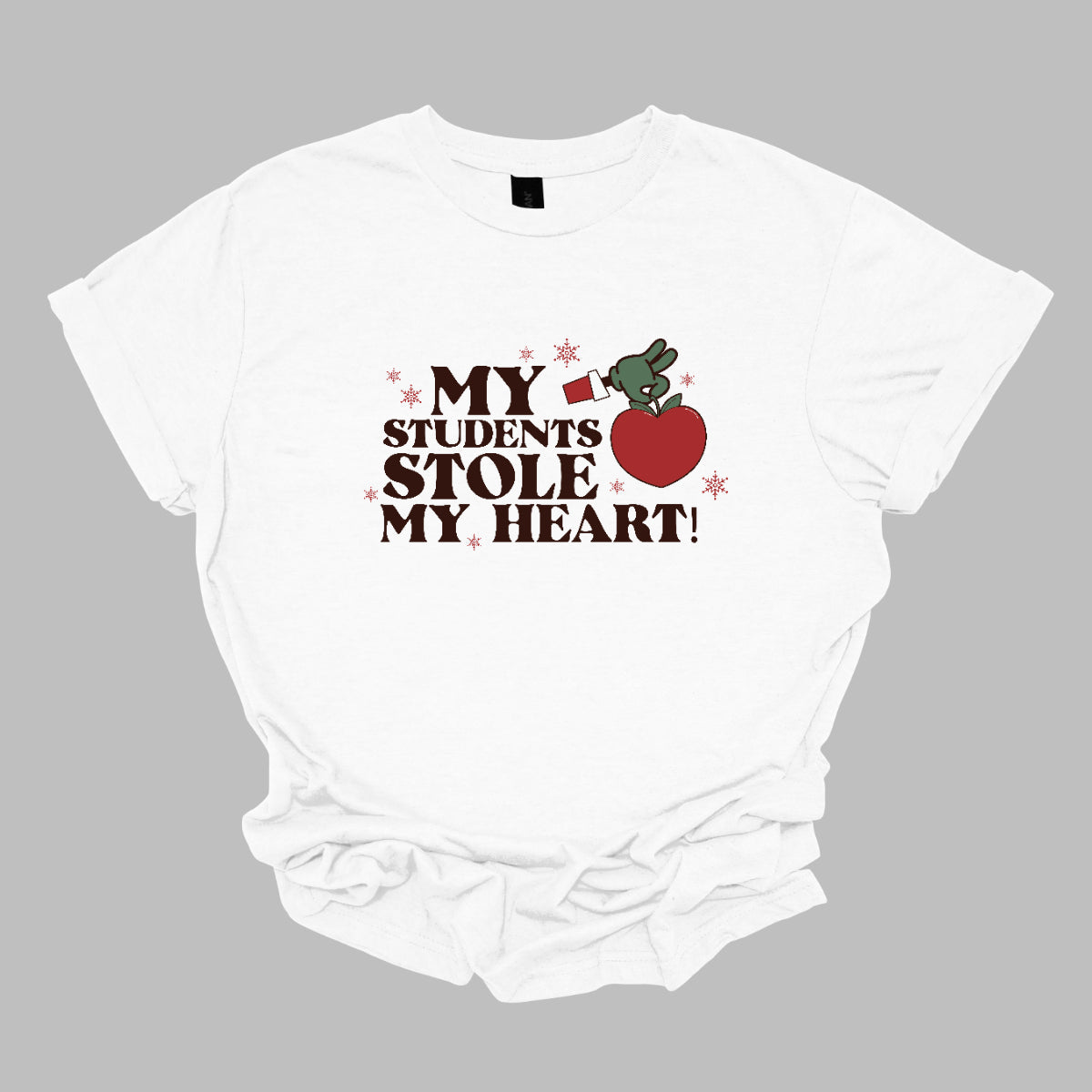 This playful t-shirt features the phrase "My students stole my heart" in fun, whimsical lettering that captures the spirit of teaching. Below the text, a cheeky illustration of the Grinch's green arm emerges, playfully grasping a shiny red apple, symbolizing knowledge and education. Shop at Gorgeousware.com