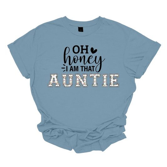 The shirt design features the phrase "Oh Honey, I'm That Auntie" in a playful and eye-catching style. The word "Auntie" is written in bold, bubbly letters filled with intricate floral patterns, giving it a soft and feminine touch. The rest of the phrase uses a mix of fun, whimsical fonts to create a lively and energetic feel. The design is perfect for a stylish and confident auntie who loves to embrace her role with charm and humor. Shop Gorgeouseware.com