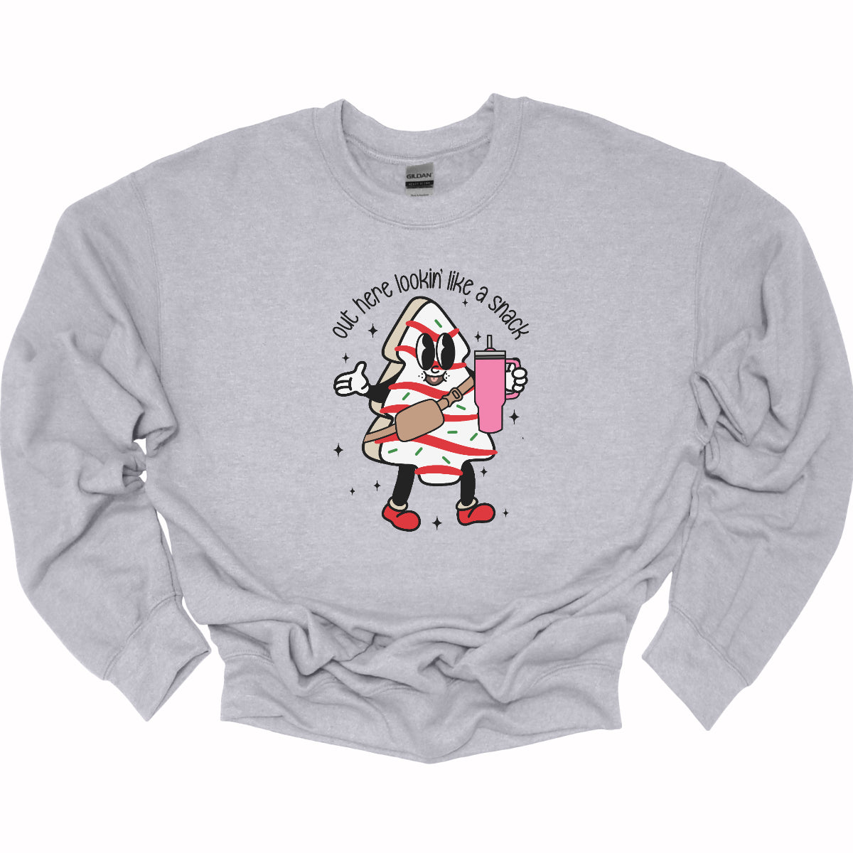 This playful t-shirt features the phrase "Out here lookin' like a snack" in a bold black stick figure font, giving it a fun and casual vibe. Beneath the text, a charming cartoon Christmas tree cake adds a whimsical touch, complete with a cheerful smiling face, a stylish belt bag, and a cup. The surrounding sparkles enhance the festive spirit, making this shirt a delightful choice for spreading holiday cheer with a humorous twist! Shop Gorgeousware.com