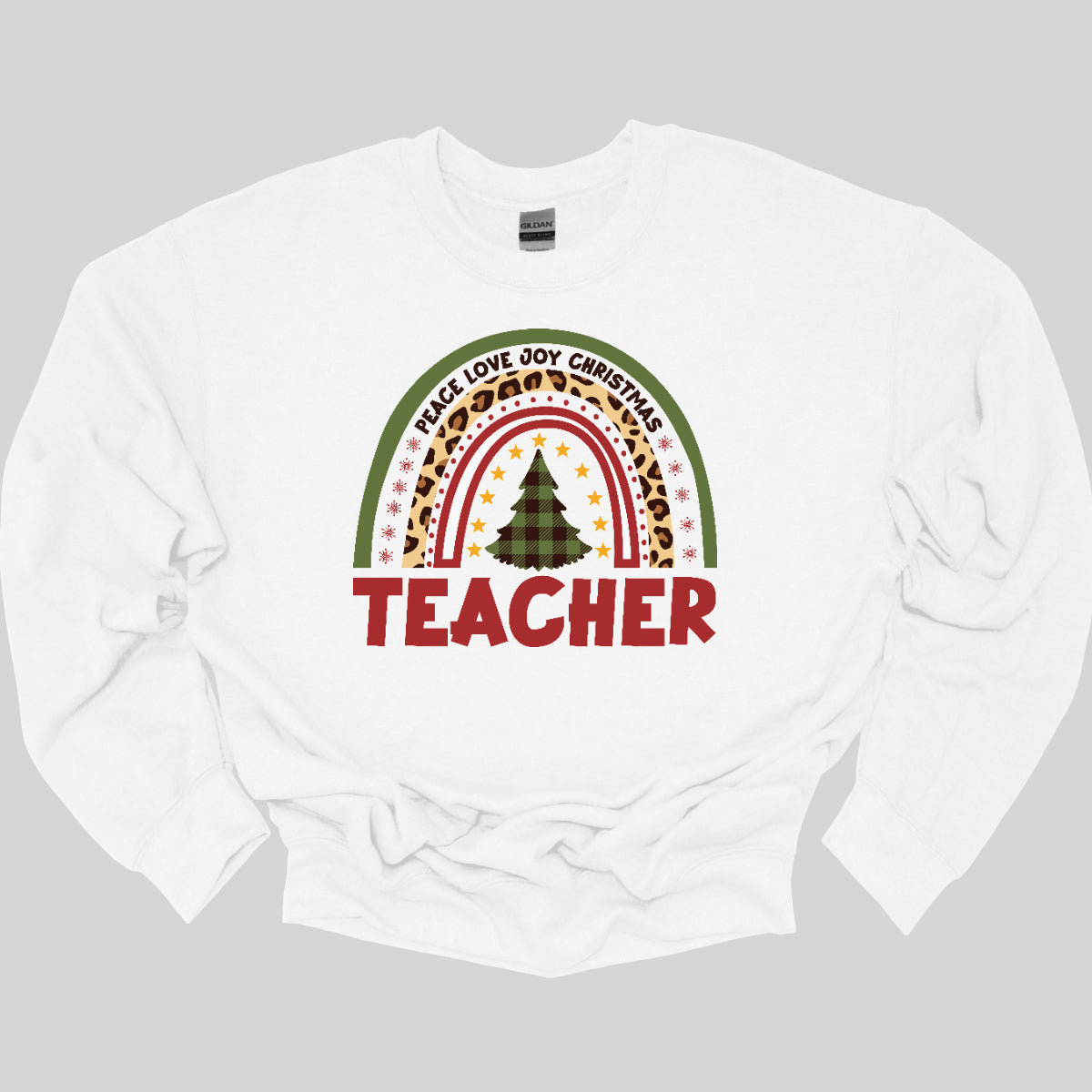 The t-shirt design features a vibrant, patterned rainbow that arcs gracefully across the fabric. Each color of the rainbow is adorned with playful patterns, such as polka dots, snowflakes, and cheetah print, adding a whimsical touch. At the center of the rainbow stands a beautifully illustrated Christmas tree. Shop at orgeousware.com