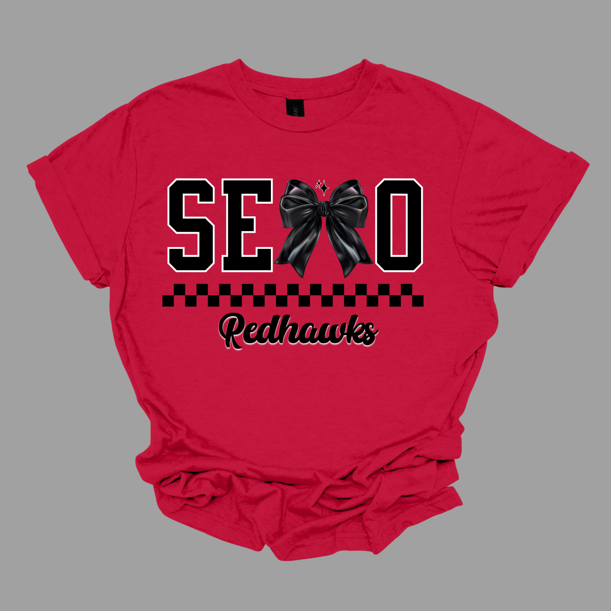Show off your SEMO pride in style with this trendy short sleeve t-shirt! Featuring the bold letters "SEMO," where the "M" is cleverly replaced by a stylish black croquette bow, this shirt adds a unique twist to your wardrobe. Underneath, a playful checkerboard stripe adds a fun touch, while "Redhawks" is elegantly written in a cute cursive font, bringing a touch of flair. Shop at Gorgeousware.com