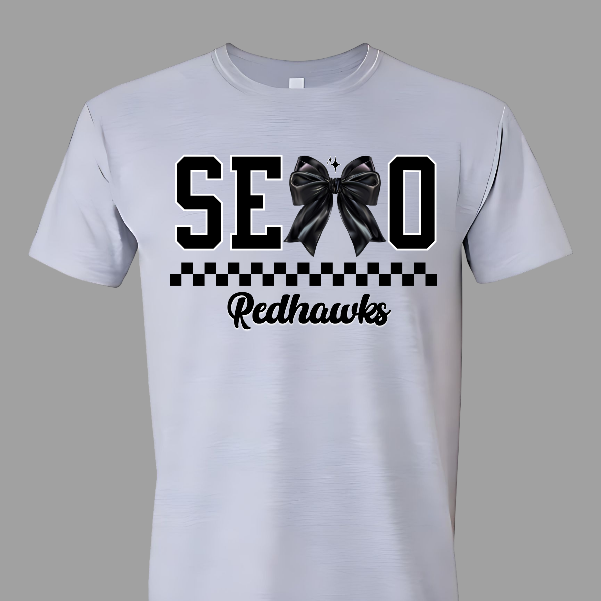 Show off your SEMO pride in style with this trendy short sleeve t-shirt! Featuring the bold letters "SEMO," where the "M" is cleverly replaced by a stylish black croquette bow, this shirt adds a unique twist to your wardrobe. Underneath, a playful checkerboard stripe adds a fun touch, while "Redhawks" is elegantly written in a cute cursive font, bringing a touch of flair. Shop at Gorgeousware.com