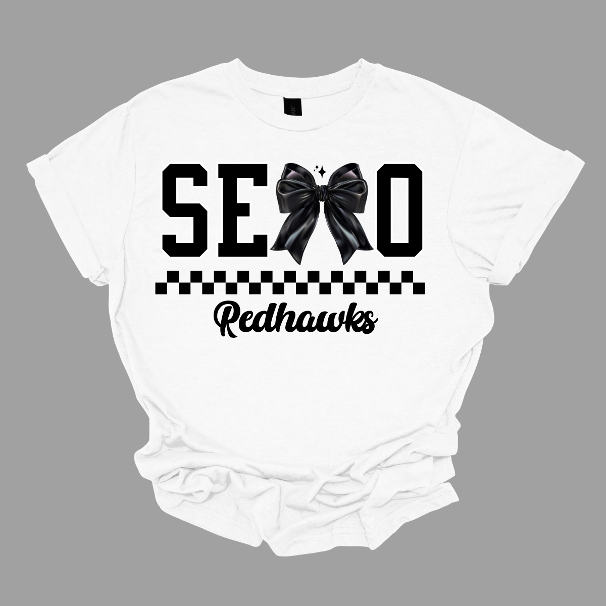 Show off your SEMO pride in style with this trendy short sleeve t-shirt! Featuring the bold letters "SEMO," where the "M" is cleverly replaced by a stylish black croquette bow, this shirt adds a unique twist to your wardrobe. Underneath, a playful checkerboard stripe adds a fun touch, while "Redhawks" is elegantly written in a cute cursive font, bringing a touch of flair. Shop at Gorgeousware.com