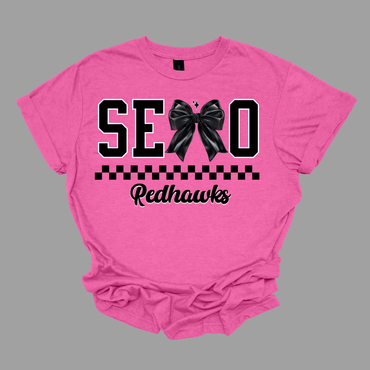 Show off your SEMO pride in style with this trendy short sleeve t-shirt! Featuring the bold letters "SEMO," where the "M" is cleverly replaced by a stylish black croquette bow, this shirt adds a unique twist to your wardrobe. Underneath, a playful checkerboard stripe adds a fun touch, while "Redhawks" is elegantly written in a cute cursive font, bringing a touch of flair. Shop at Gorgeousware.com