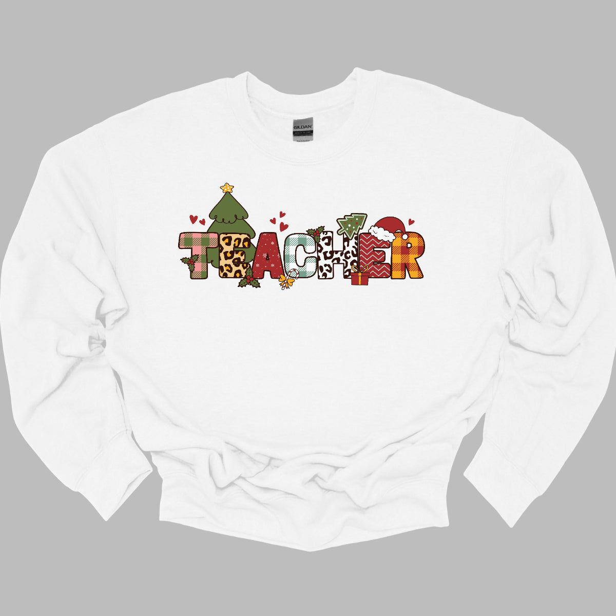 This eye-catching t-shirt boldly displays the word "TEACHER" in large block letters, each letter showcasing a unique style of print that adds a fun and creative flair. Behind the first "E," a cheerful Christmas tree adds a festive touch, while the second "E" is adorned with a cute Santa hat, making it even more playful. Shop Gorgeouswre.com