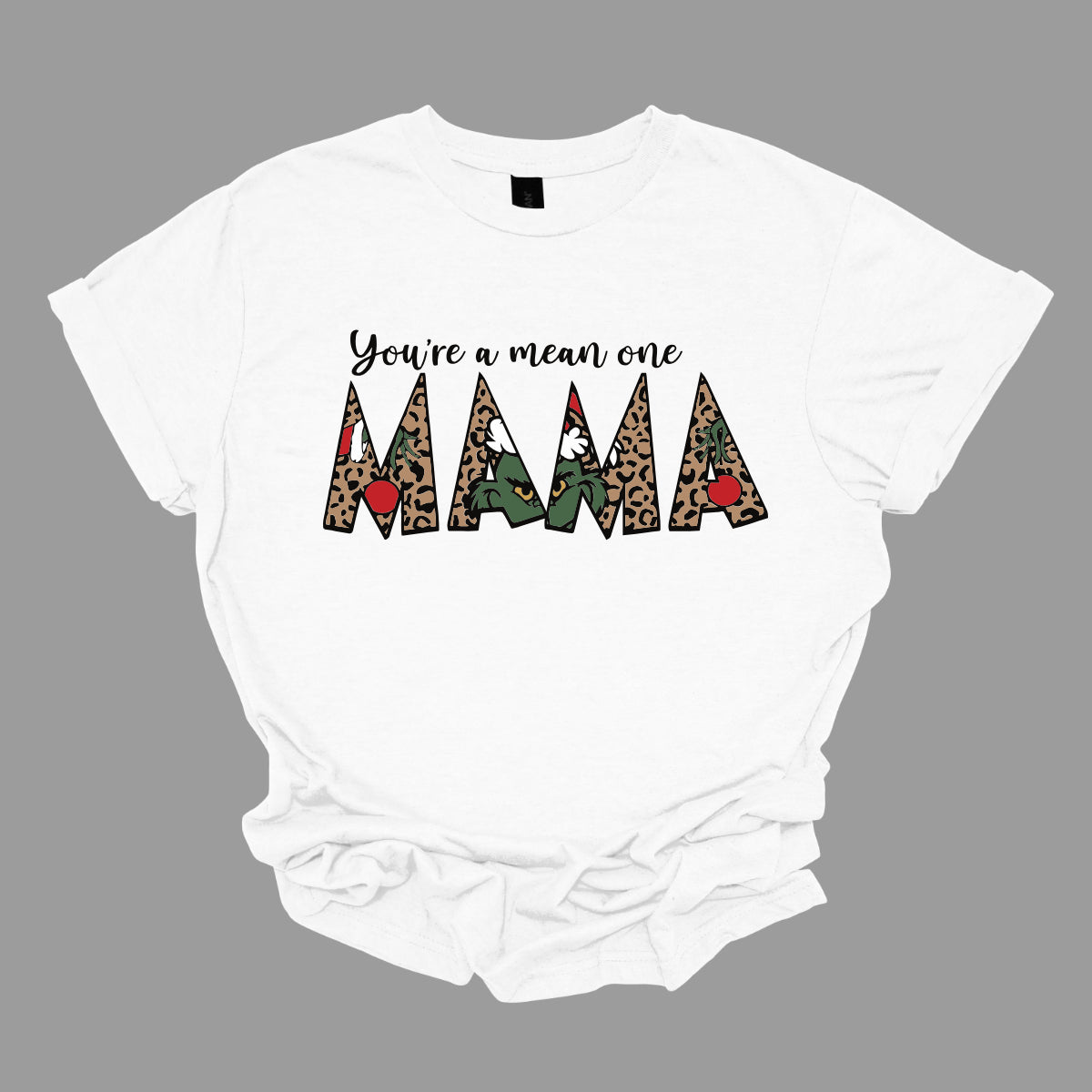The phrase "You're a Mean One Mama" takes center stage, with "You're a Mean One" written in elegant black cursive font that flows beautifully across the fabric. The standout element is the word "Mama," which is rendered in bold, eye-catching letters. Each letter of "Mama" is filled with a quirky depiction of the Grinch, set against a vibrant cheetah print background. Shop Gorgeousware.com