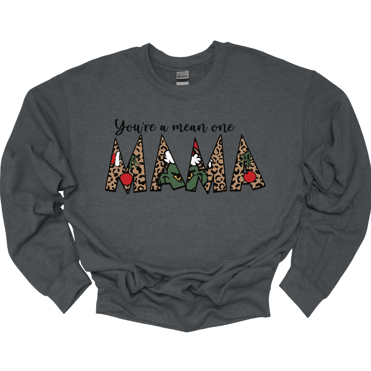 The phrase "You're a Mean One Mama" takes center stage, with "You're a Mean One" written in elegant black cursive font that flows beautifully across the fabric. The standout element is the word "Mama," which is rendered in bold, eye-catching letters. Each letter of "Mama" is filled with a quirky depiction of the Grinch, set against a vibrant cheetah print background. Shop Gorgeousware.com