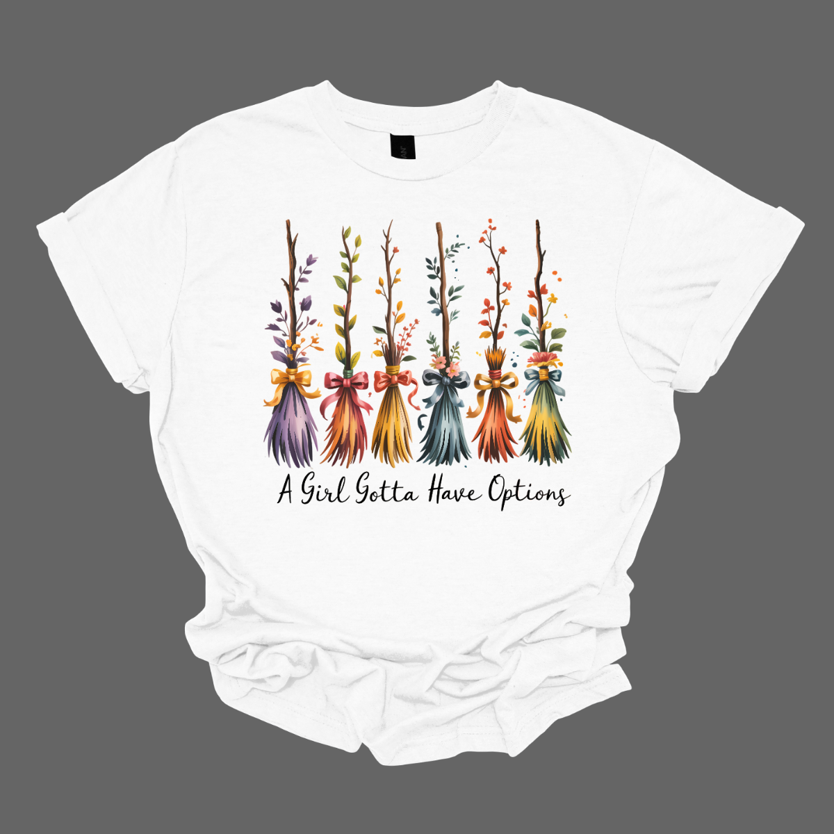 Add a little magic to your fall wardrobe with this fun and whimsical Halloween-inspired tee! The design features six wispy brooms lined up in playful autumn colors, each with its own unique charm. Beneath them, the phrase “A Girl Gotta Have Options” is written, making this shirt a cheeky and stylish nod to witchy fall vibes. Shop at Gorgeousware.com