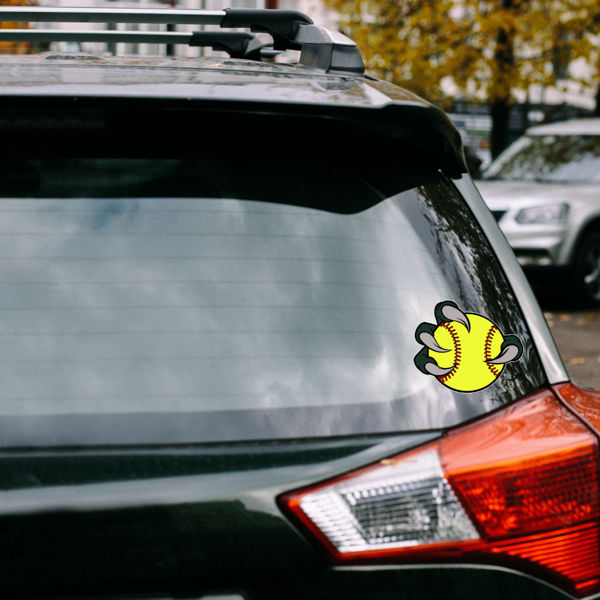 Car with a softball-themed sticker on the rear window, parked outdoors.