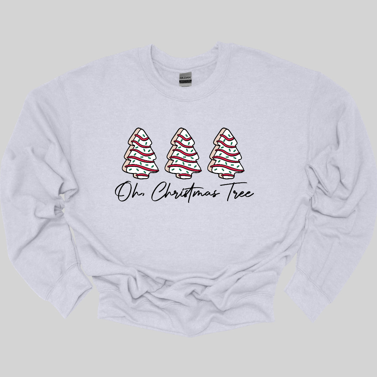 This t-shirt features a whimsical holiday design that’s perfect for spreading cheer. The shirt is adorned with the phrase “Oh Christmas Tree” written in elegant black cursive font, adding a touch of sophistication to the festive message. Above the words, three iconic Christmas tree snack cakes are illustrated, each depicted with their classic, playful decorations. Shop Gorgeousware.com