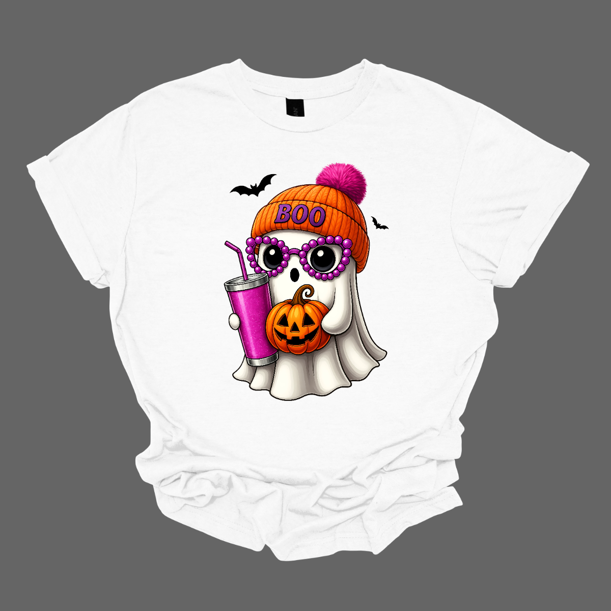 Bring on the spooky-cute vibes with this adorable fall tee! 👻🎃 The design features a sweet little ghost bundled up in an orange sock cap with a pink pom on top. The flipped brim of the hat reads “BOO” for a playful touch. This stylish ghost also sports purple reading glasses, holds a matching purple drink cup, and carries a tiny jack-o’-lantern bucket — ready for all the fall fun! Two little bats flutter in the background to complete the whimsical Halloween scene. Gorgeousware.com