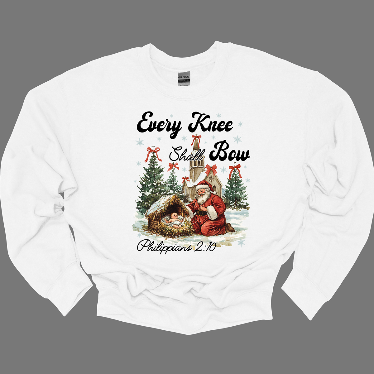 This festive and powerful apparel design features the phrase "Every Knee Shall Bow" in bold, elegant lettering, symbolizing the reverence and humility of the Christmas story. The artwork showcases Santa Claus, traditionally known for his joyful spirit, bowing down in awe before a humble manger that cradles baby Jesus. In the background, an old chapel stands as a symbol of faith, with evergreen trees adorned with festive bows, adding a touch of seasonal beauty and serenity.  Shop at Gorgeousware.com