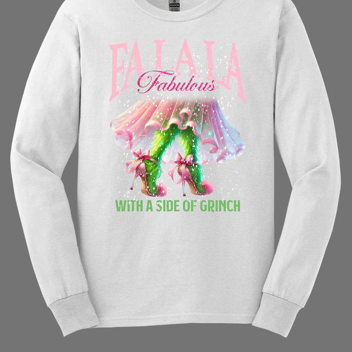 The design features a playful and festive take on the Grinch character with a stylish twist. The phrase "Fa La La Fabulous" is at the top in a fun, cursive font with a bouncy, holiday-inspired feel. The word "Fabulous" stands out in bold, glamorous lettering with subtle sparkles, giving it a chic vibe. Below, the Grinch is shown with her girly green legs, styled in light pink high heels adorned with oversized bows at the back, adding a sweet and fashionable touch. Shop at Gorgeousware.com