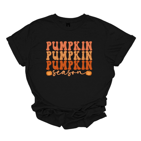 The t-shirt design features the phrase "Pumpkin Pumpkin Pumpkin Season" in a playful and eye-catching layout. At the top, the word "Pumpkin" is repeated three times, each instance stacked vertically. Each "Pumpkin" is rendered in a bold, attention-grabbing font, with each pumpkin in a progressively darker shade of orange. This gradient effect gives depth and dimension to the design, highlighting the seasonal theme. Shop Gorgeaousware.com