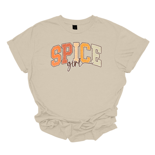 The t-shirt features the phrase "Spice Girl" in a visually striking layout. The word "Spice" is prominently displayed in big, bold retro-style letters. The letters are adorned in varying shades of orange, that captures the warmth and vibrancy of autumn. Beneath "Spice," the word "Girl" is elegantly styled in a smaller, flowing cursive font. Shop Gorgeousware.com