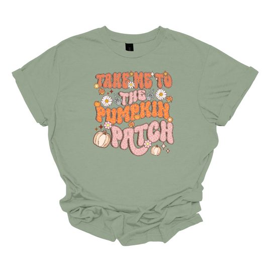 The t-shirt design features the playful phrase "Take Me to the Pumpkin Patch" in a stylish retro font. The text is rendered in a delightful combination of orange and pink pastel cheetah print, giving it a trendy and eye-catching look with a touch of whimsy. Shop Gorgouseware.com