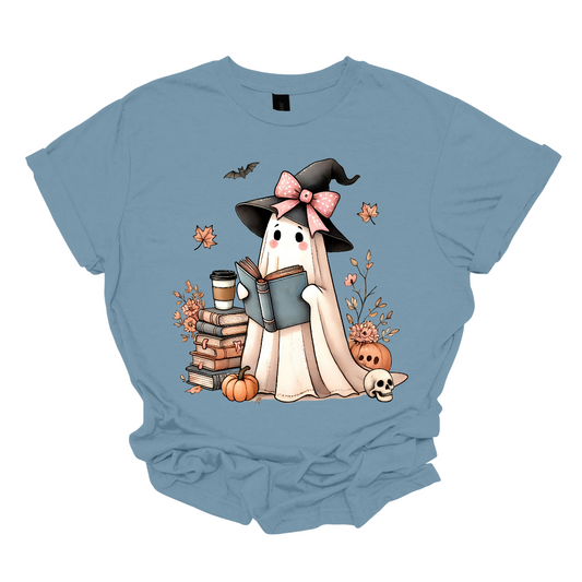 This T-shirt features an adorable ghost wearing a witch's hat adorned with a pink bow. The ghost has a warm, friendly expression as she enjoys her coffee, with a stack of books by her side.&nbsp; Around her, small pumpkins are scattered on the ground, adding a cozy, autumnal vibe. The design perfectly captures the charm of the Halloween season with a cute and whimsical twist. Shop at Gorgeousware.com