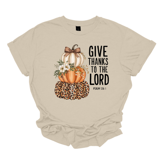 Celebrate the season of gratitude with this beautiful fall graphic tee! The design features a charming stack of three pumpkins — cream, orange, and leopard print — topped with a bow and accented with soft cream-colored flowers between the second and third pumpkin. To the right, in bold lettering, the verse “Give thanks to the Lord – Psalms 136:1” is displayed, making this the perfect faith-inspired fall shirt. Shop at Gorgeousware.com