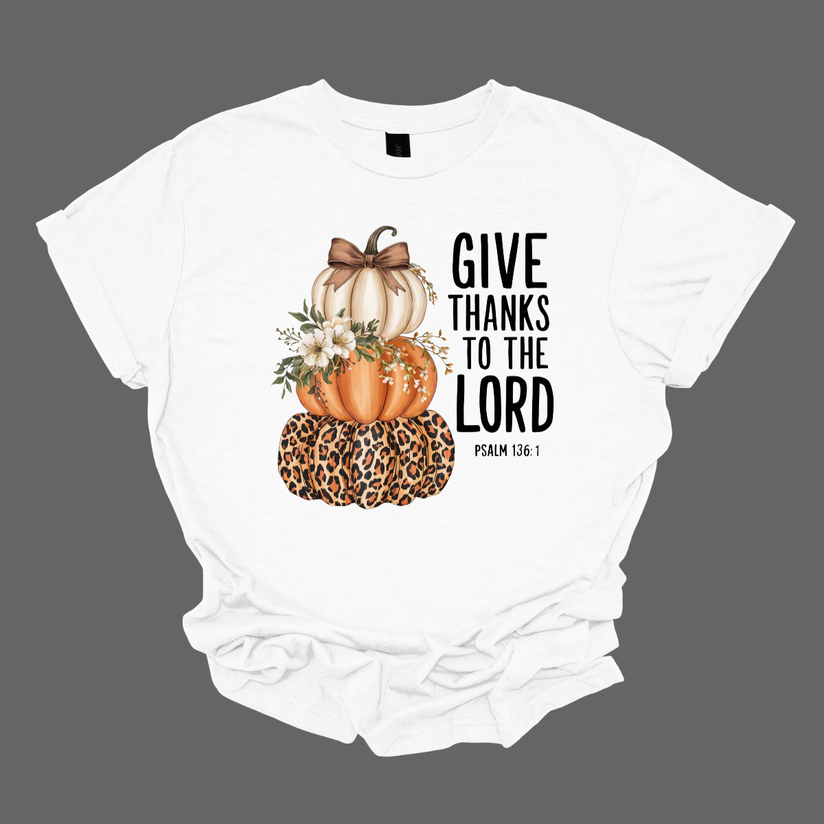 Celebrate the season of gratitude with this beautiful fall graphic tee! The design features a charming stack of three pumpkins — cream, orange, and leopard print — topped with a bow and accented with soft cream-colored flowers between the second and third pumpkin. To the right, in bold lettering, the verse “Give thanks to the Lord – Psalms 136:1” is displayed, making this the perfect faith-inspired fall shirt. Shop at Gorgeousware.com