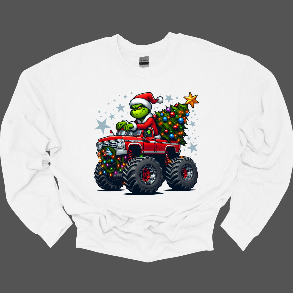 White sweat shirt with a graphic of a Grinch driving a monster truck with a Christmas tree, on a grey background. Shop at Gorgeousware.com