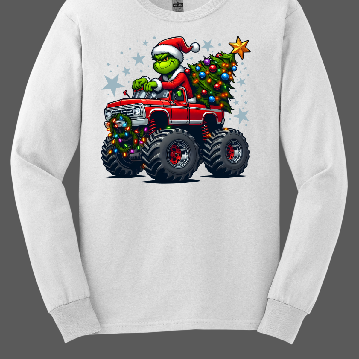 White long-sleeve shirt with a graphic of a Grinch driving a monster truck with a Christmas tree, on a gray background. Shop at Gorgeousware.com