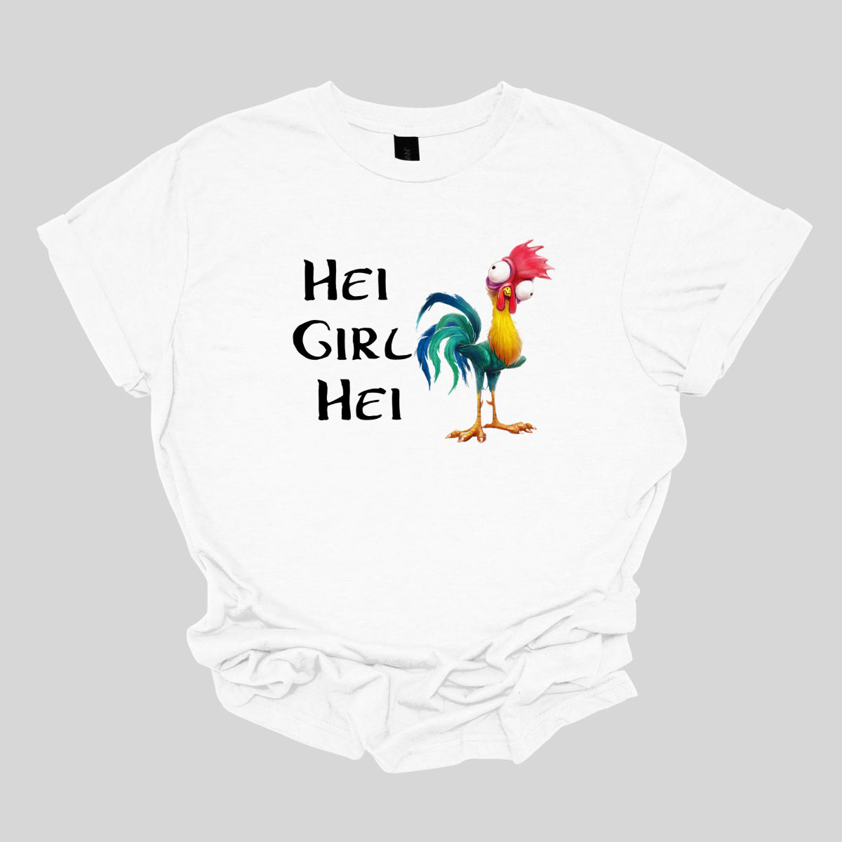 This t-shirt features a playful and vibrant design with the phrase "Hei Girl Hei" emblazoned in a lively, cartoonish black font that adds a fun and energetic touch. The words are arranged in a way that captures attention and conveys a cheerful message.&nbsp;Next to the text is the charming cartoon character Hei Hei from Disney's Moana. Hei Hei is depicted with his usual goofy expression and colorful plumage, bringing a whimsical and endearing element to the design. Shop Gorgeousware.com